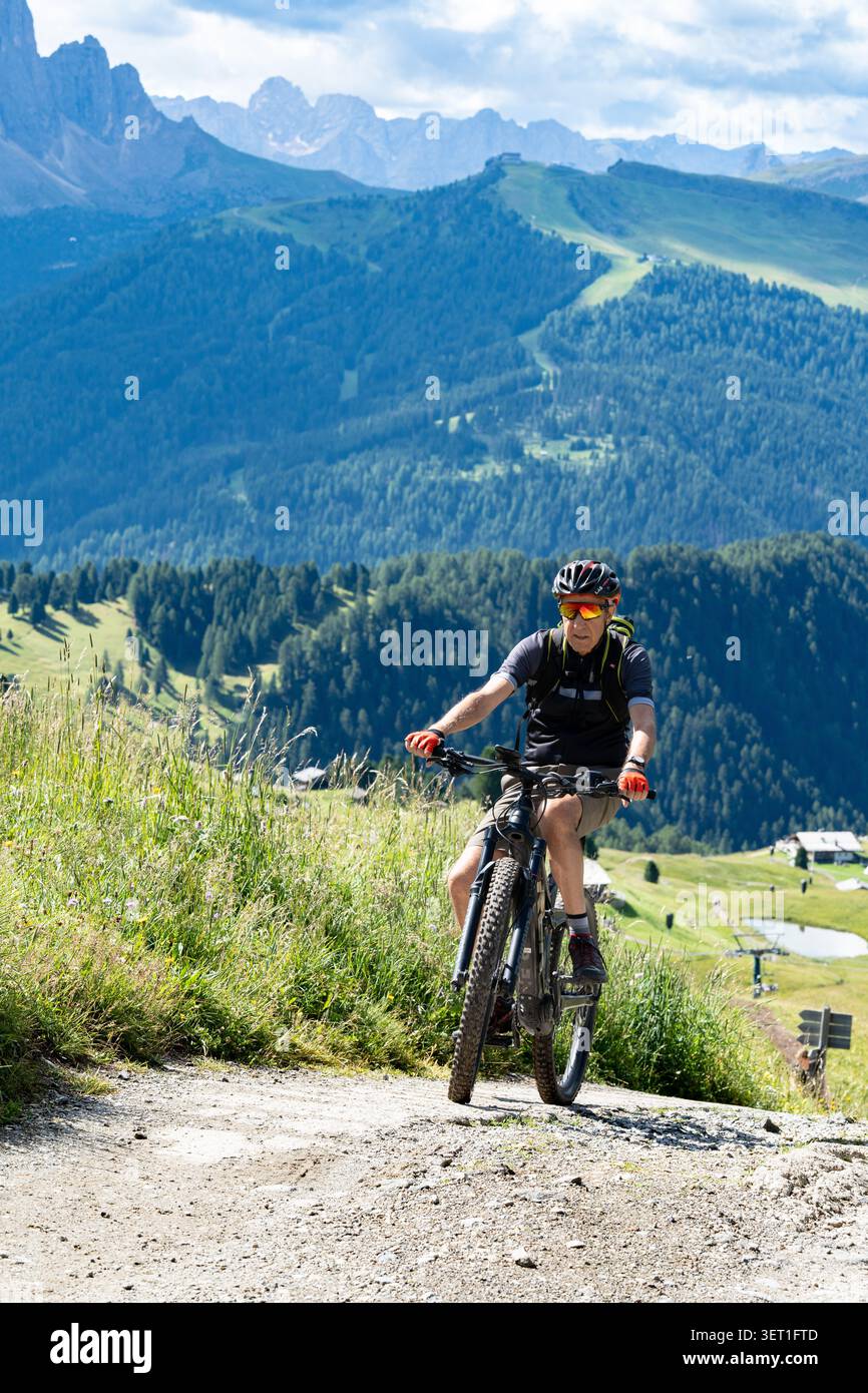 Ortisei, Italia - 22 luglio 2025: Senior man in sella a una mountain bike elettrica su un sentiero ghiaioso nelle Dolomiti Foto Stock