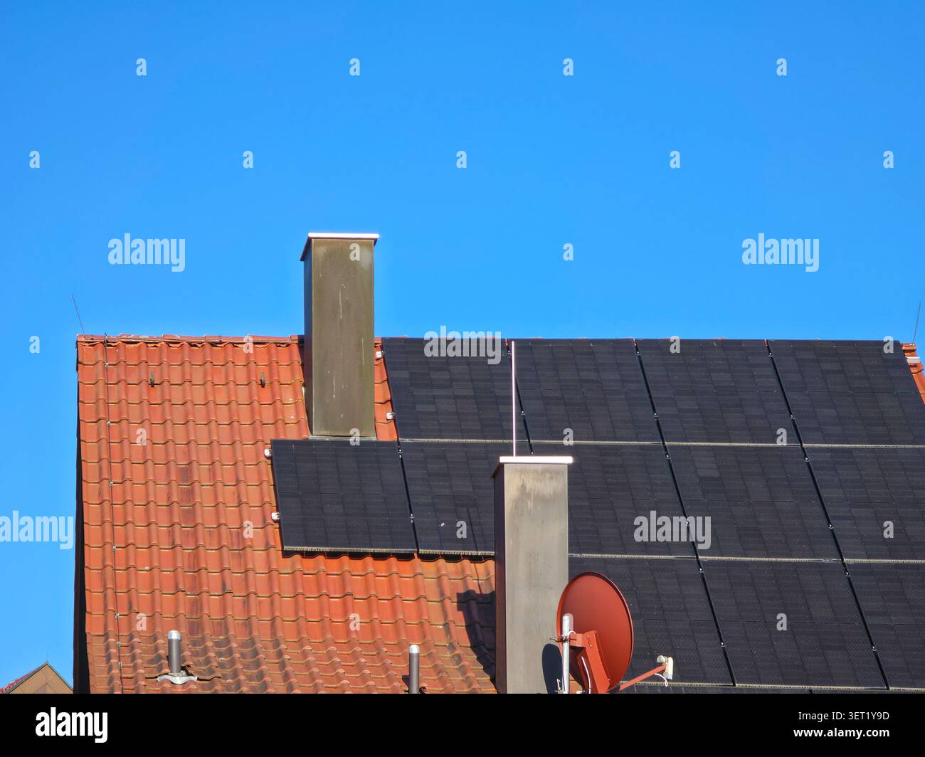 molti moduli fotovoltaici che coprono il lato sud del tetto rosso con camini che massimizzano la potenza solare sotto il cielo blu Foto Stock
