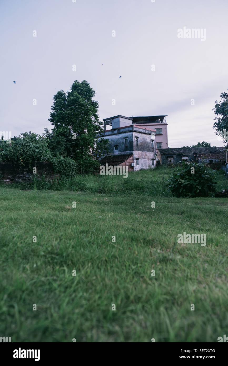 Una casa a piu' piani con moderne aggiunte sul tetto si erge dietro lussureggianti prati verdi e alberi Foto Stock