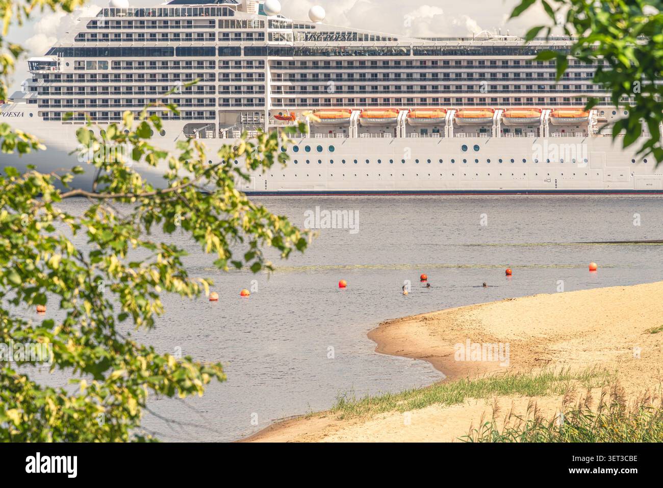 Vita estiva lungo il fiume con persone che si rilassano su una spiaggia della città mentre una nave da crociera MSC passa lungo il fiume Daugava a riga, in Lettonia. Foto Stock