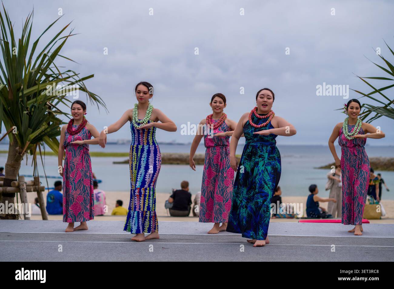 Le donne che si esibiscono in un tradizionale Hula hawaiano ballano su un palco da spiaggia, indossando abiti floreali colorati e leis durante un festival culturale all'aperto. Foto Stock