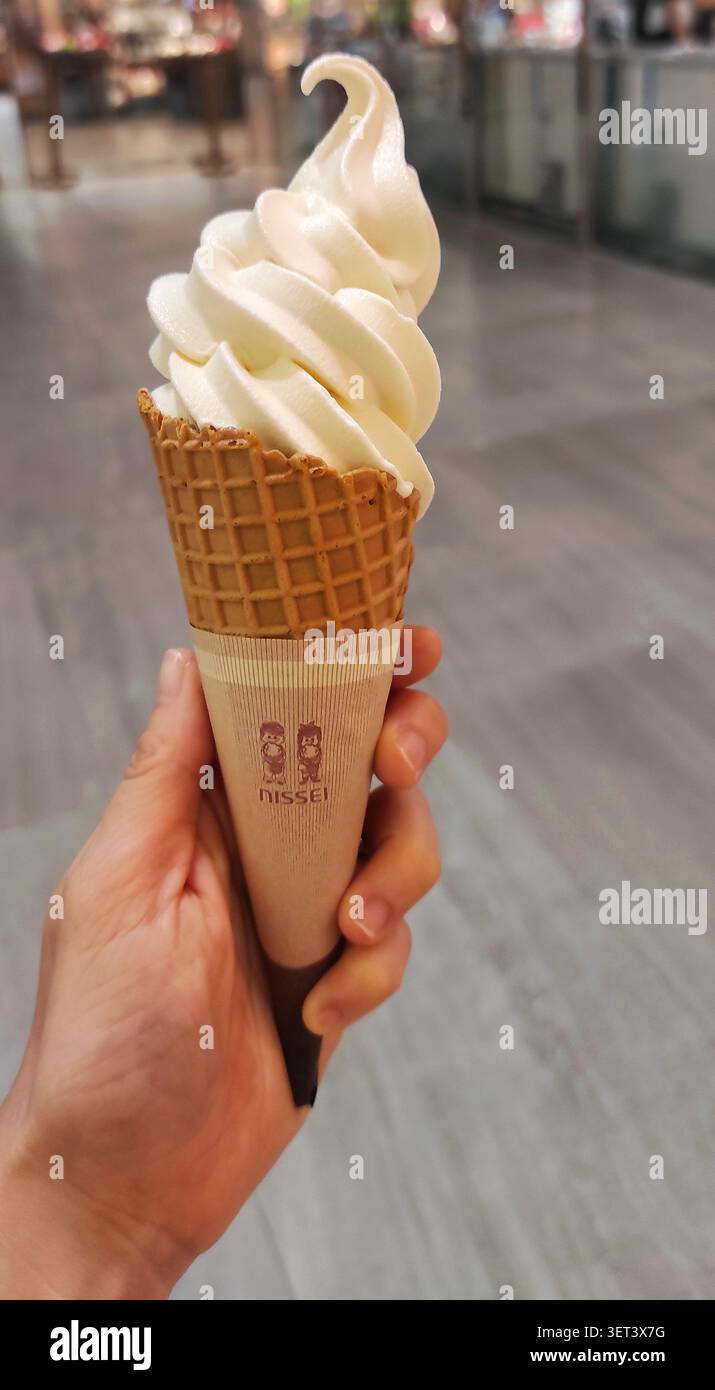 HONG KONG - 20 LUGLIO 2023: Una mano tiene in mano un cono di gelato alla vaniglia con un involucro a marchio NISSEI in una galleria di negozi. Foto Stock