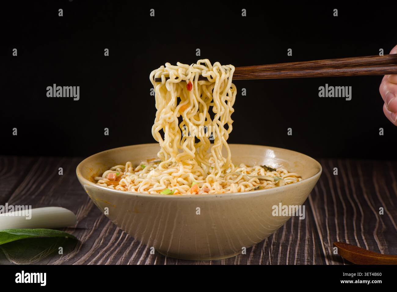 Sollevare a mano il ramen istantaneo da una ciotola con le bacchette su un tavolo di legno scuro Foto Stock