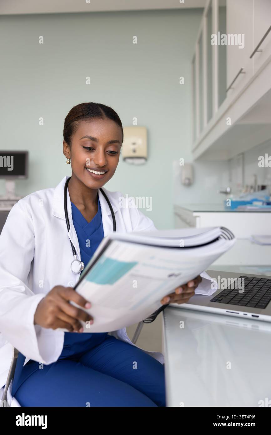 Positivo giovane donna afroamericana medico che esamina un grande libro di testo Foto Stock