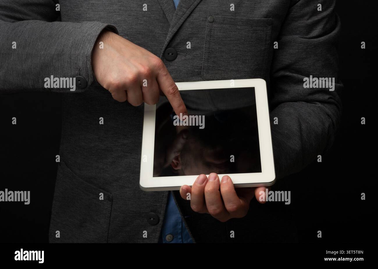 Persona che punta verso il tablet mentre indossa un abbigliamento formale su sfondo scuro Foto Stock