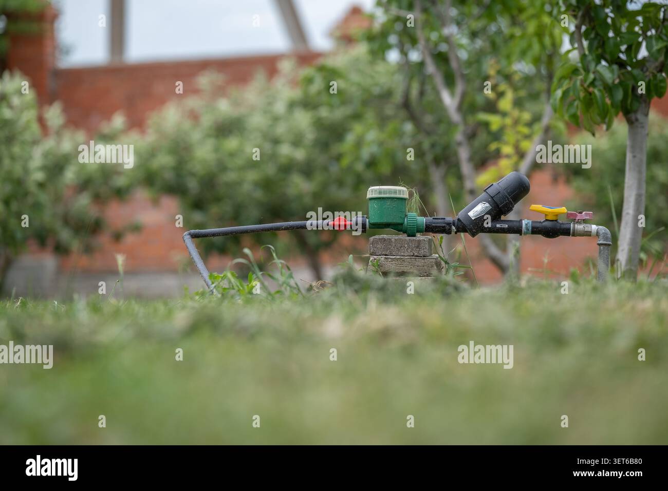 Vista da terra di un'unità di controllo dell'irrigazione a goccia con filtro, valvola e componenti di distribuzione dell'acqua installati in un giardino residenziale. L'immagine Foto Stock