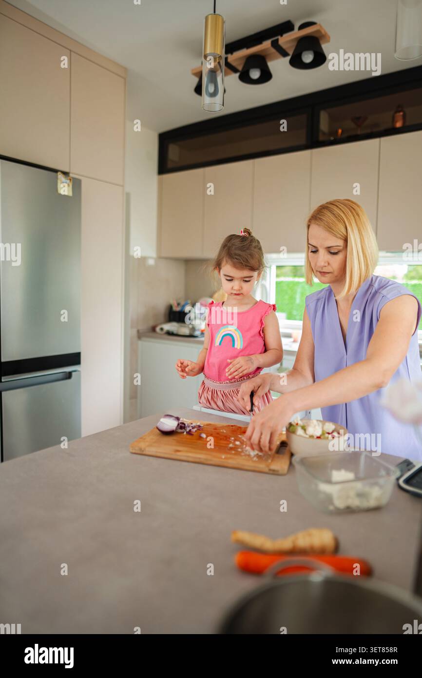 Madre e figlia cucinano insieme in una cucina luminosa Foto Stock