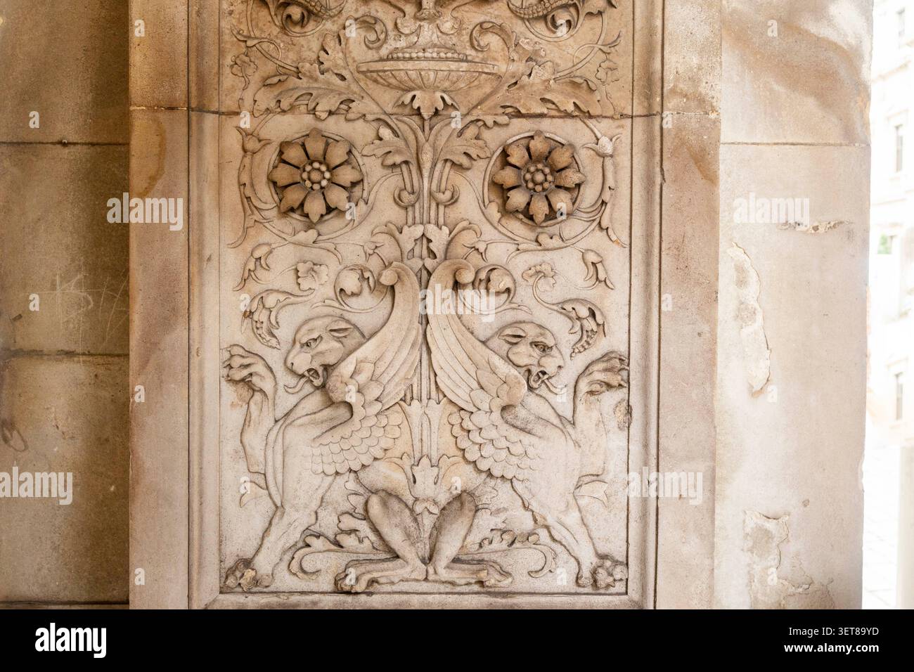 Primo piano di un'antica scultura in pietra raffigurante creature mitiche alate e ornamenti floreali. Foto Stock