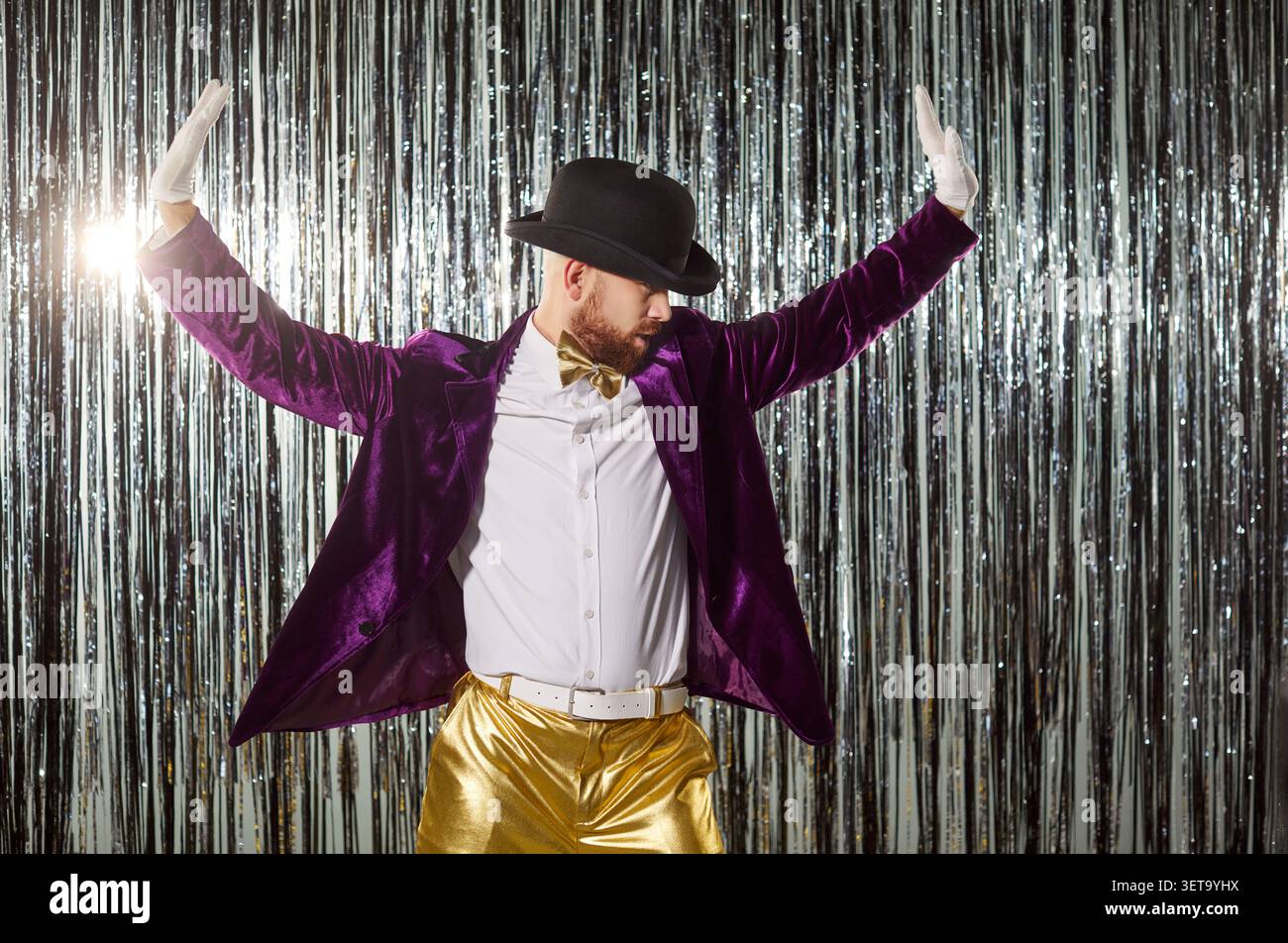 Uomo simpatico e simpatico che indossa giacca viola, pantaloni dorati, cappello, guanti che ballano energicamente in performance Foto Stock
