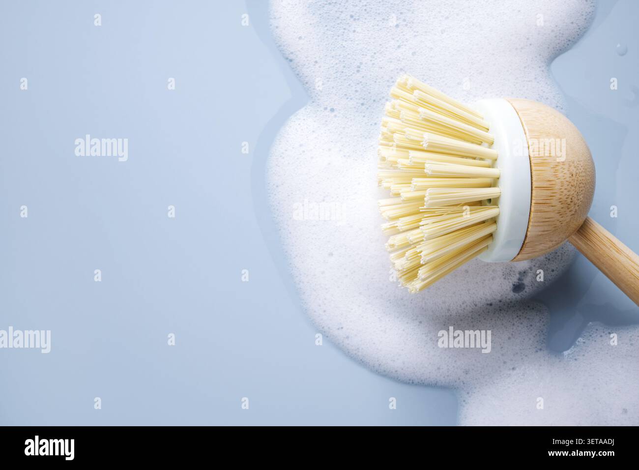 Spazzola in bambù per lavastoviglie con schiuma di sapone e bolle di sapone su sfondo blu Foto Stock