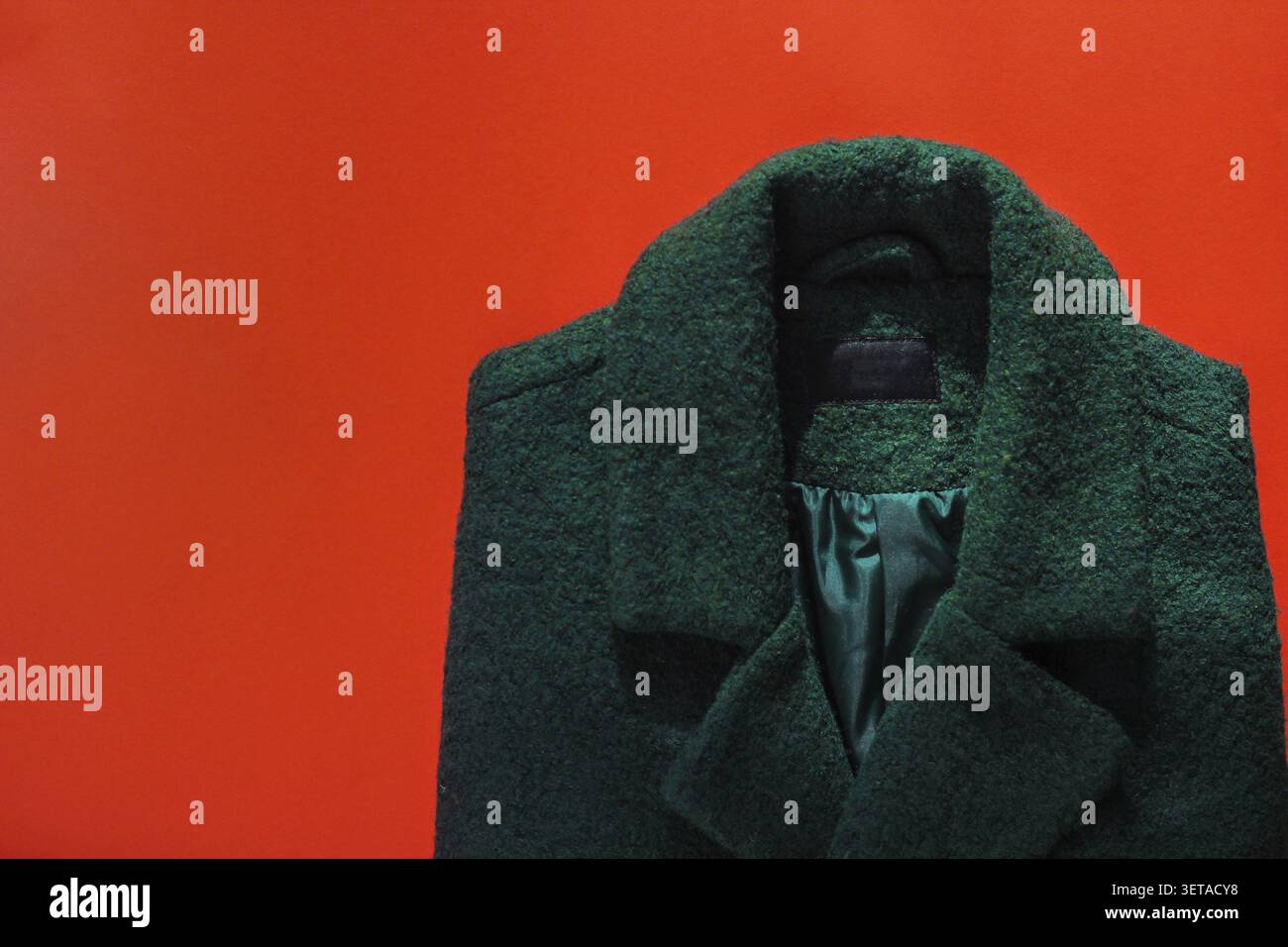 Cappotto verde da donna su sfondo rosso. guardaroba autunnale, vestiti caldi autunnali, posate Foto Stock