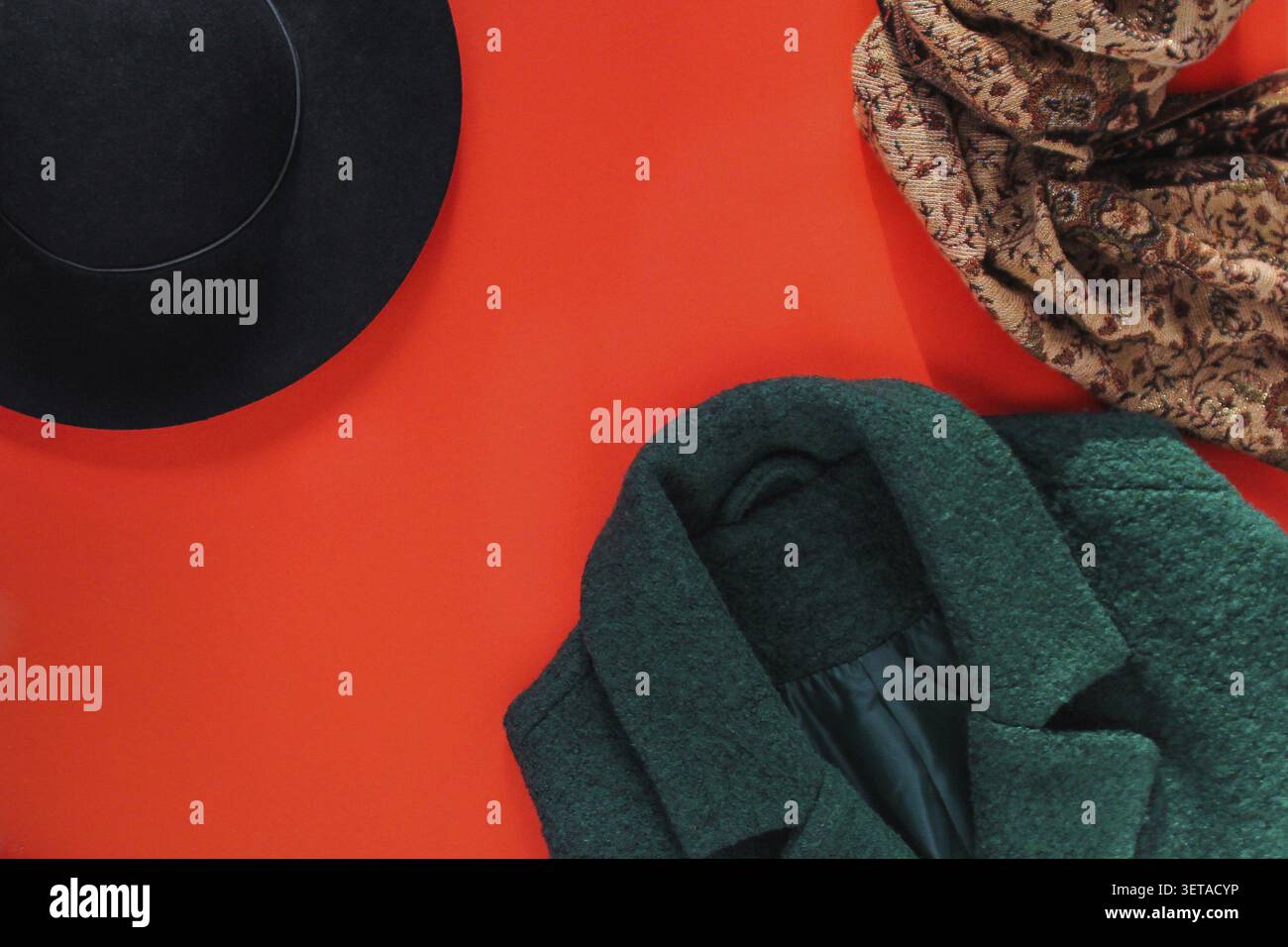 Concetto di moda autunnale. Abbigliamento elegante da donna. Cappotto da donna verde, cappello nero e sciarpa su sfondo rosso. guardaroba autunnale, abiti caldi autunnali, posate, Foto Stock