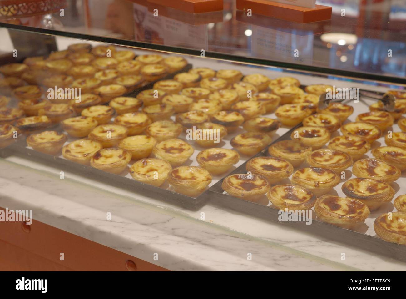File di Pastéis de nata portoghese Custard Tarts appena sfornata su vassoi in metallo dietro il banco della panetteria in vetro Foto Stock