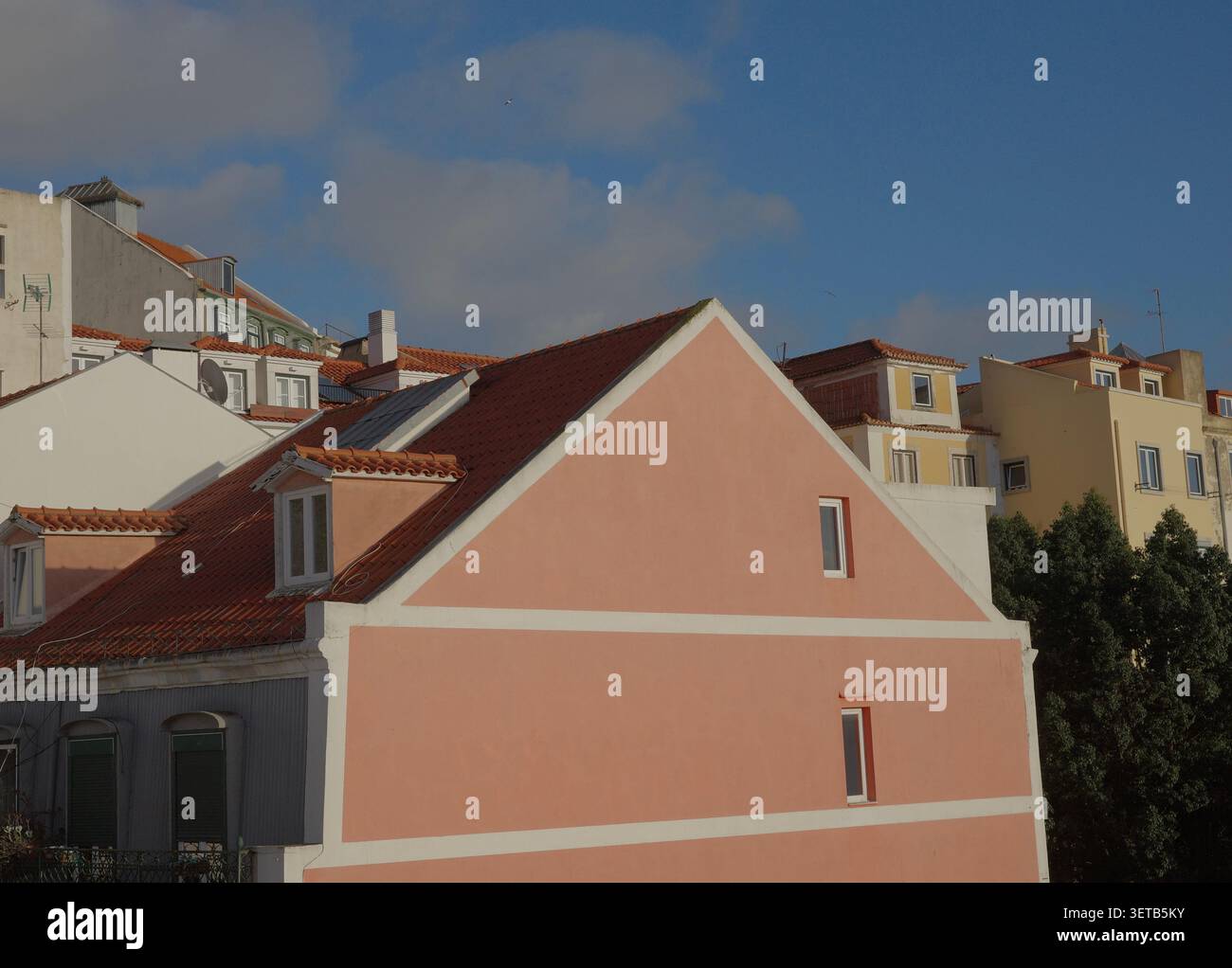 Colorati edifici color pastello con tetti in terracotta sul lato Hillside di Lisbona, Casa con tetto a spiovente rosa in primo piano contro il cielo blu Foto Stock