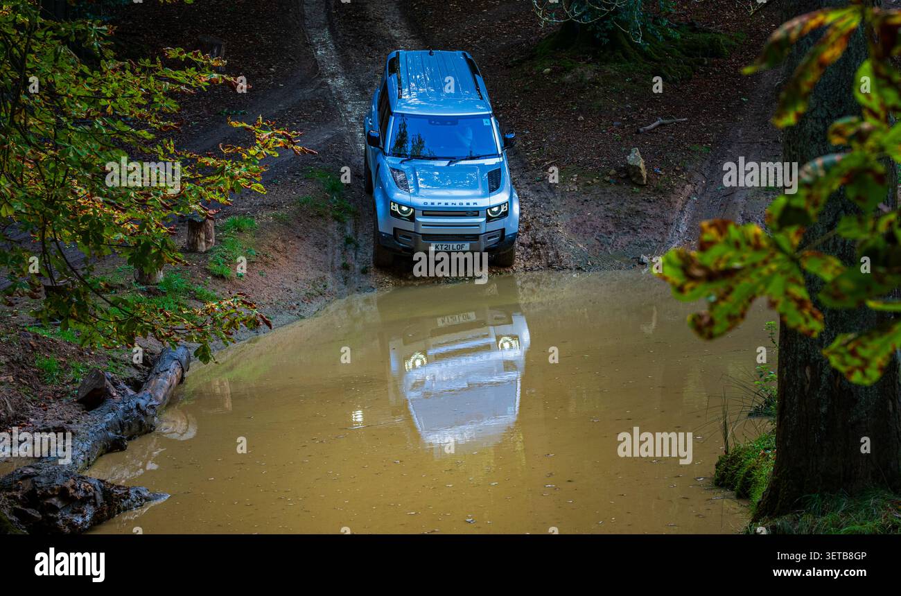 Land Rover Discovery si avvicina a un attraversamento in acque profonde durante un'esperienza di guida fuoristrada 4x4 sotto gli alberi boschivi Foto Stock