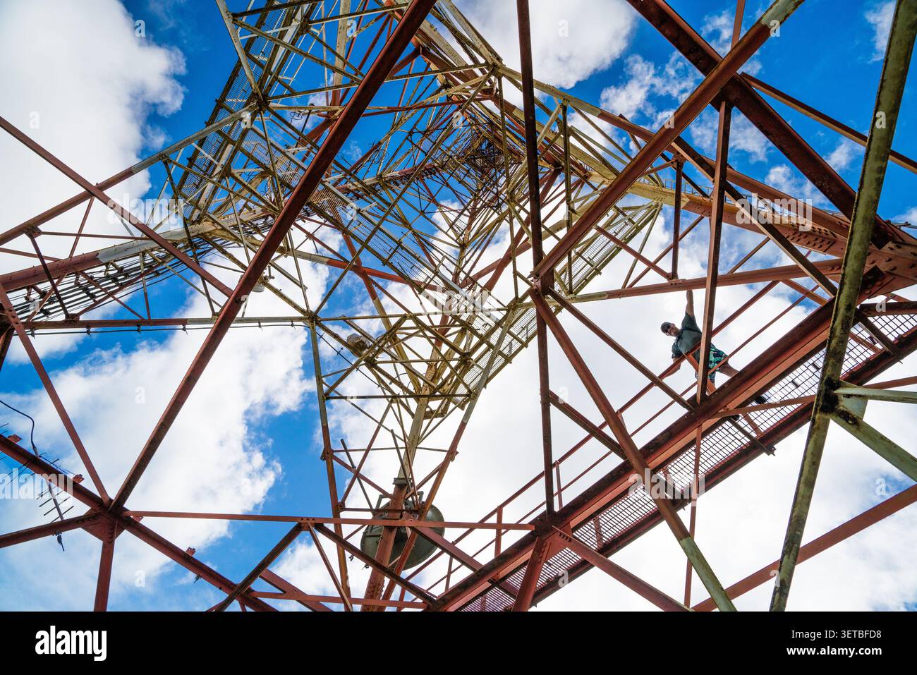 Uomo che sale da sotto una grande torre di trasmissione in acciaio Foto Stock