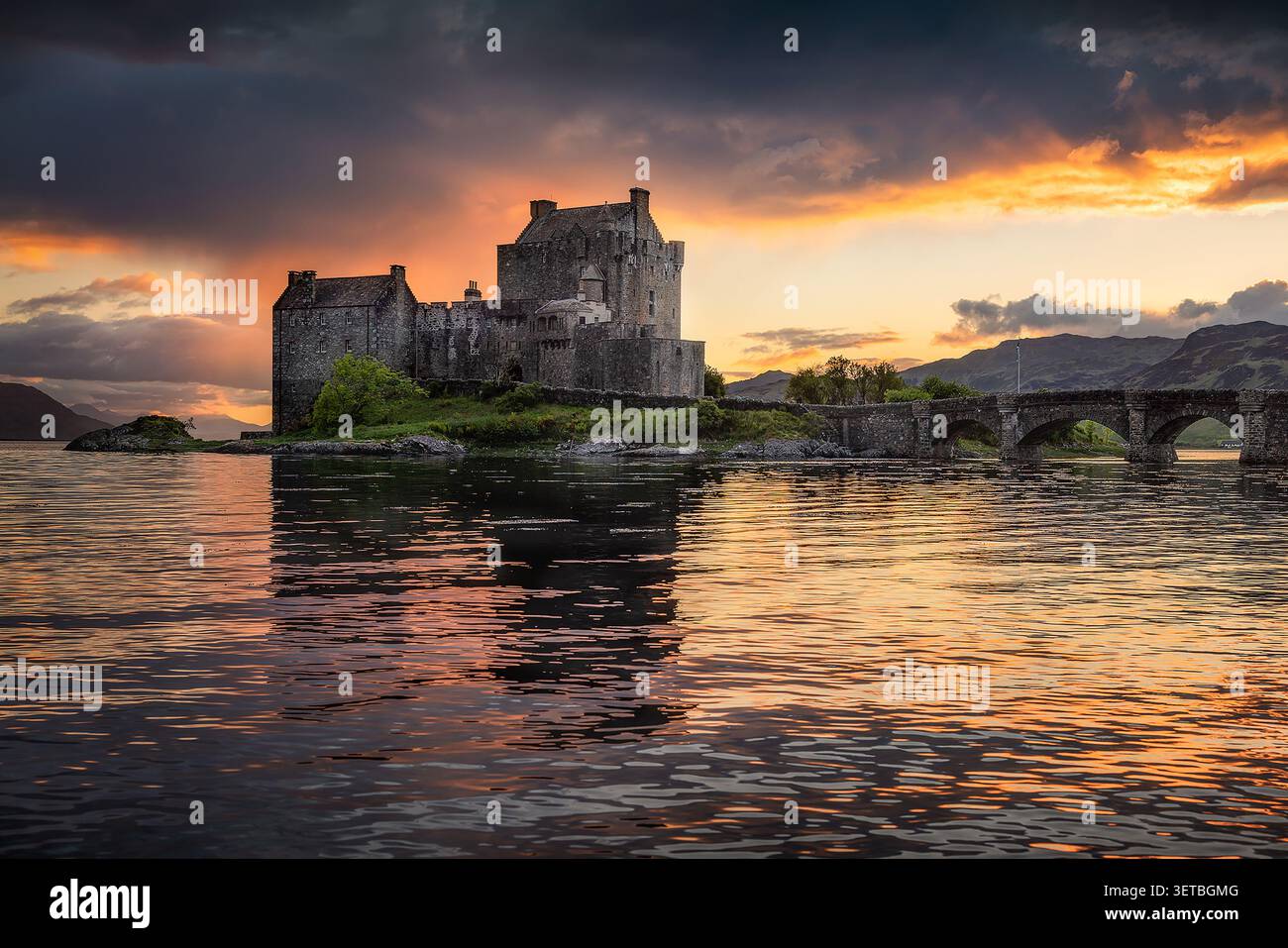 Vista del castello di Eilean Donan al tramonto con un ponte di pietra e riflessi sull'acqua a Dornie, Scozia, Regno Unito. Foto Stock