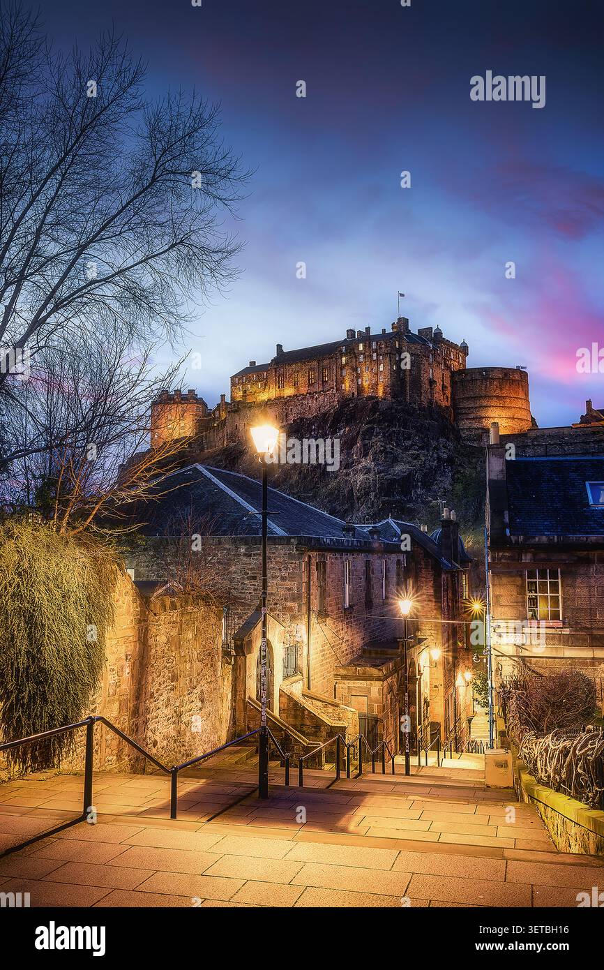 Vista del castello di Edimburgo illuminato al crepuscolo sopra edifici storici in pietra e una scala stradale a Edimburgo, Scozia, Regno Unito. Foto Stock