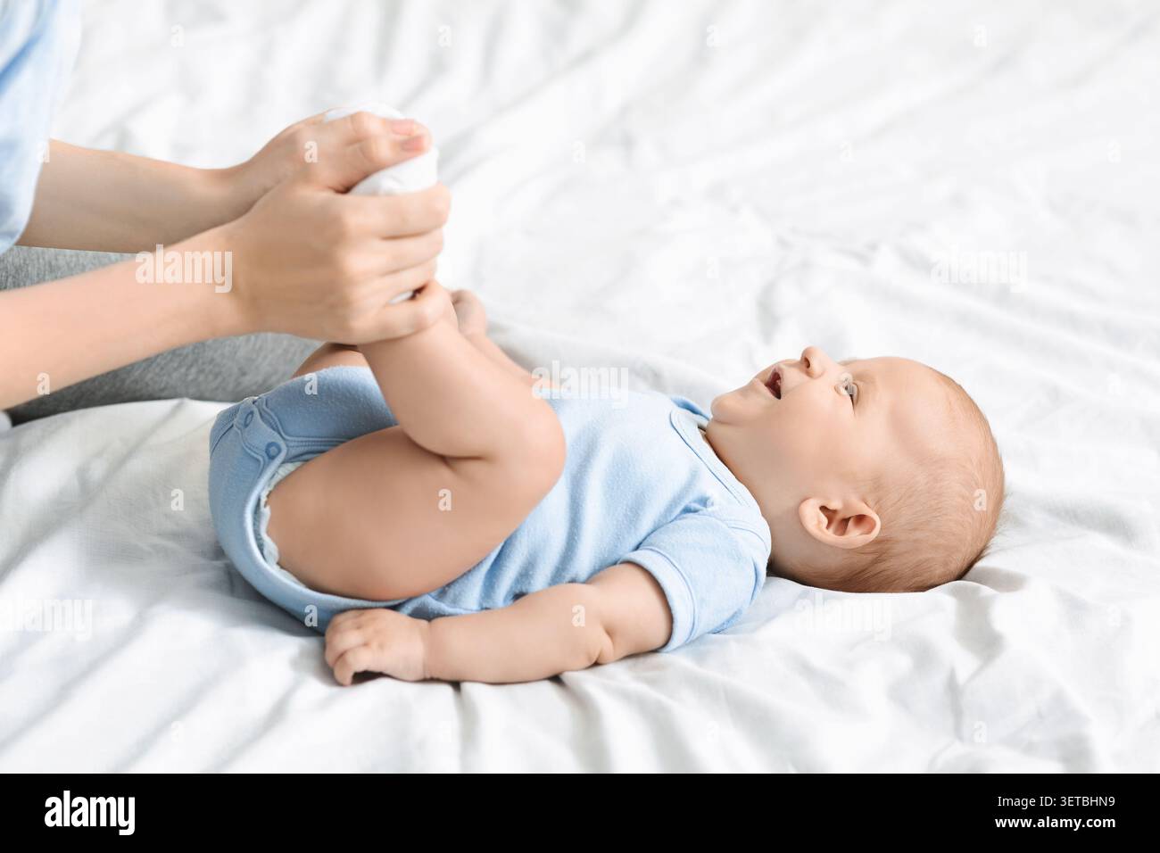 Un genitore attento che cambia il pannolino per bambini su un letto morbido con luce del mattino serena Foto Stock