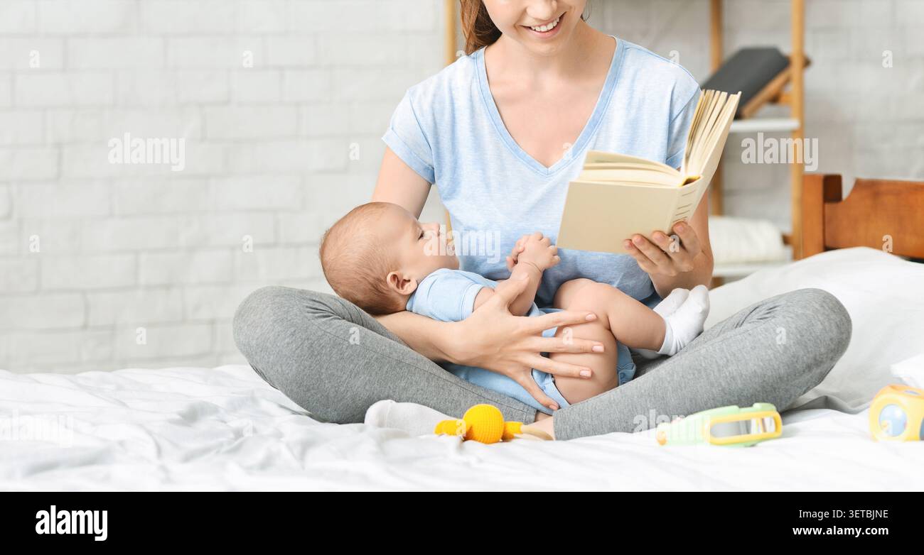 Madre che legge un libro al suo bambino seduto sul letto in una camera accogliente Foto Stock