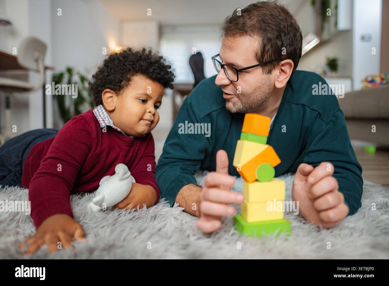 Padre e figlio giocano con blocchi colorati su tappeto Foto Stock