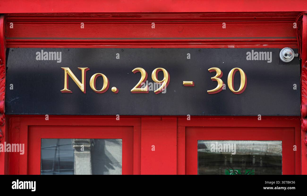 Dettaglio della facciata vintage del fronte commerciale irlandese con cornici in legno dipinte al cremisi e scritte in oro su una strada della città che mostra i numeri 29 e 30 Foto Stock