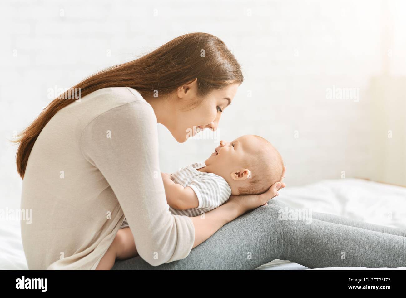 La mamma sorride con gioia all'Infant durante i momenti di legame con i morbidi letti della casa accogliente Foto Stock