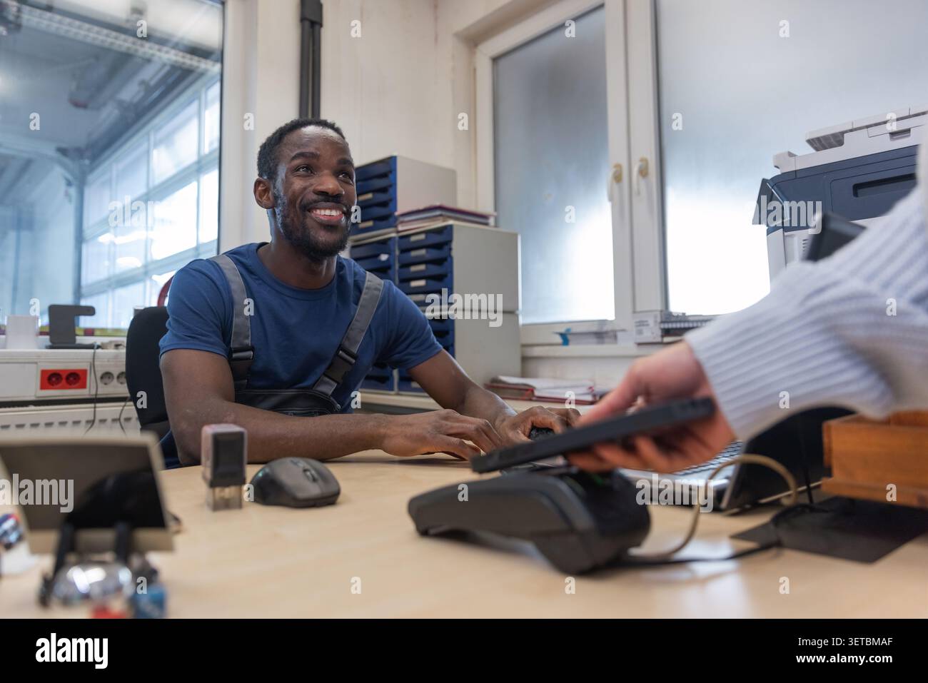 Un cliente sta pagando la riparazione di un'auto presso un'officina utilizzando una carta di credito su un terminale di pagamento. Foto Stock
