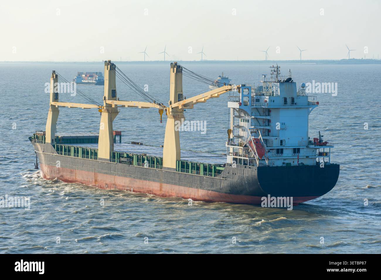Nave da carico che naviga attraverso le acque costiere vicino a Shanghai con turbine eoliche offshore all'orizzonte. Trasporto marittimo, commercio internazionale, merci Foto Stock
