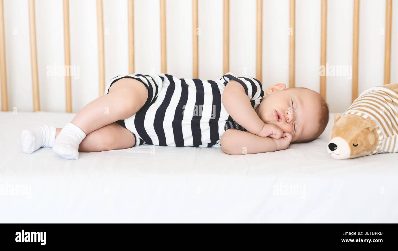 Il bambino dorme tranquillamente in una culla con un giocattolo ripieno durante il pisolino pomeridiano Foto Stock