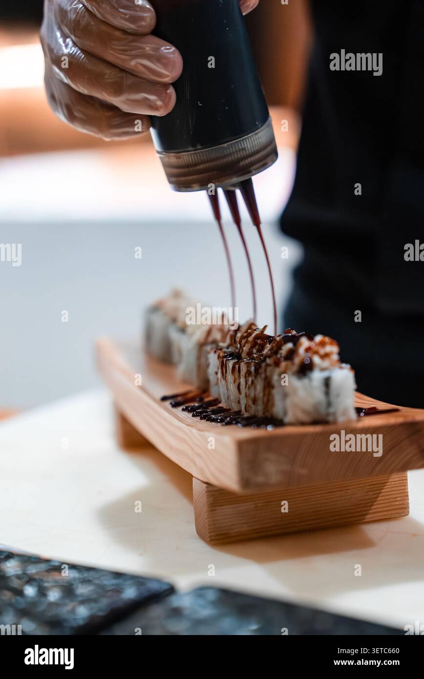 Lo chef spruzza la salsa scura sul sushi su un vassoio di legno per barche alle Maldive Foto Stock