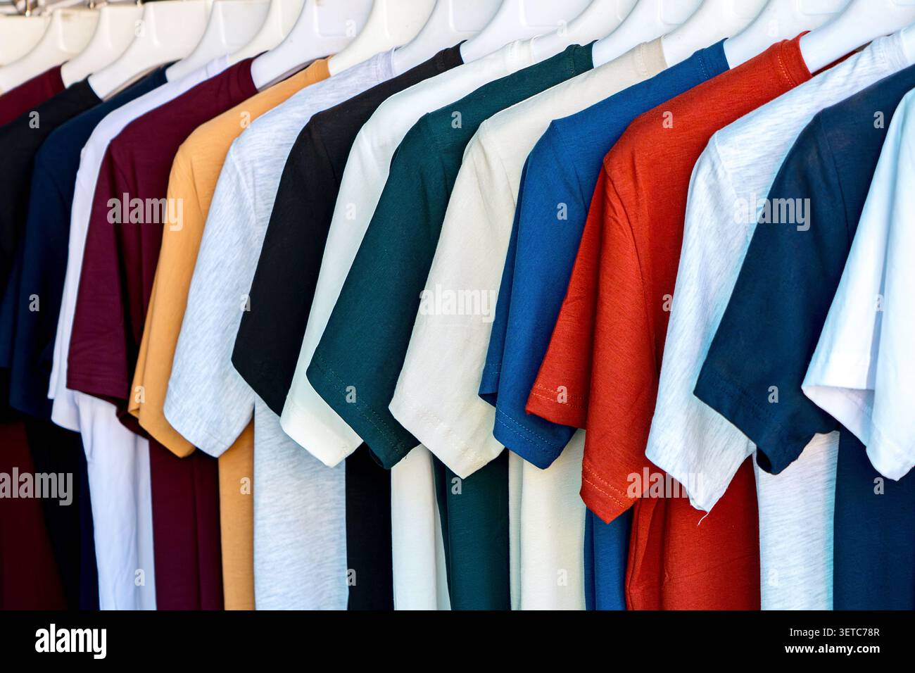 File di colorate t-shirt di cotone di base appese su un rack in un mercato di abbigliamento. Concetto: Vendita al dettaglio di massa, moda accessibile e guardaroba casual Foto Stock