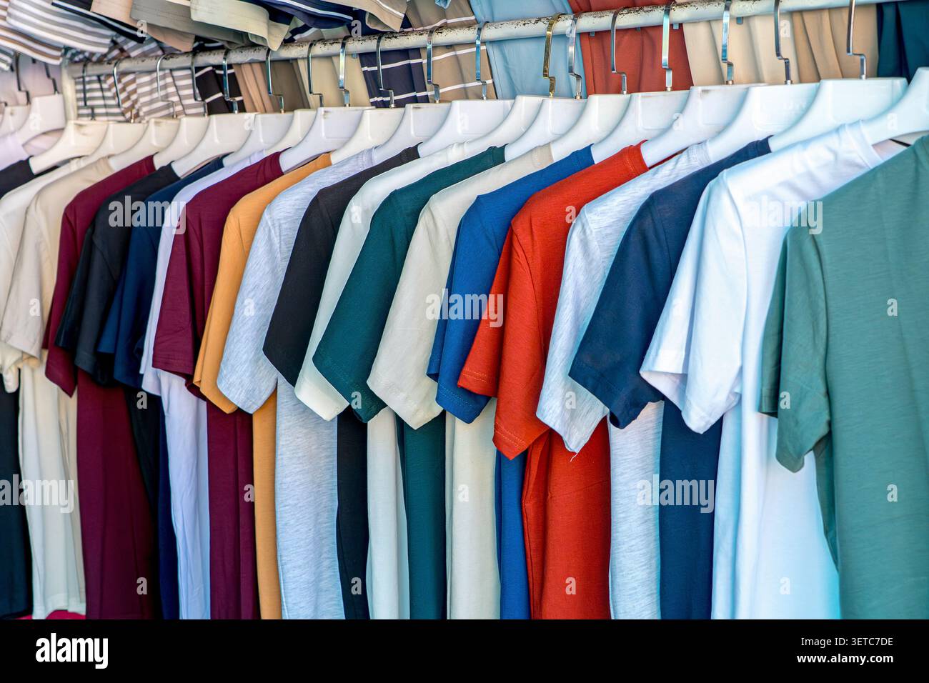File di colorate t-shirt di cotone di base appese su un rack in un mercato di abbigliamento. Concetto: Vendita al dettaglio di massa, moda accessibile e guardaroba casual Foto Stock