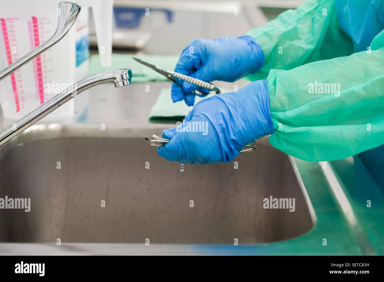 Un operatore sanitario pulisce gli strumenti chirurgici presso una stazione di lavaggio clinica, garantendo protocolli di sterilizzazione e sicurezza in ambienti chirurgici Foto Stock
