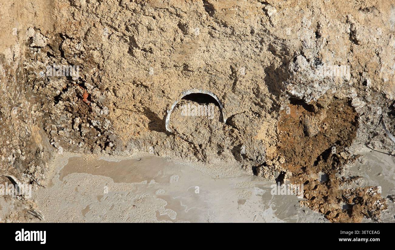 Un tubo di drenaggio danneggiato o un manicotto per cavi sporge da una parete sporca sopra un pozzo di acqua fangosa in un sito di ingegneria civile attivo Foto Stock