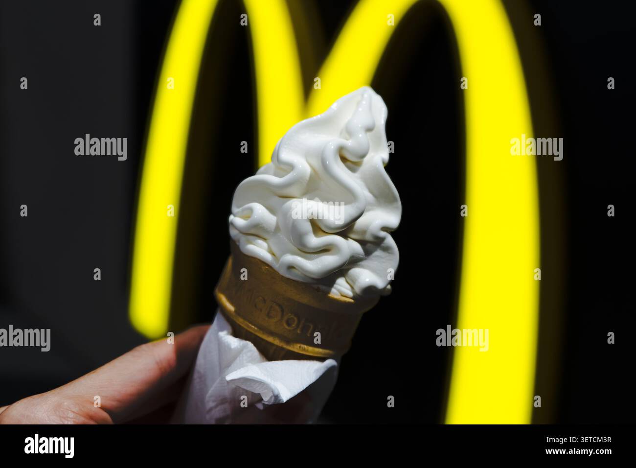 Bangkok, Thailandia - 13 settembre 2025: Un uomo che tiene un cono di gelato morbido alla vaniglia davanti al logo delle Archi dorate di McDonald's. Foto Stock