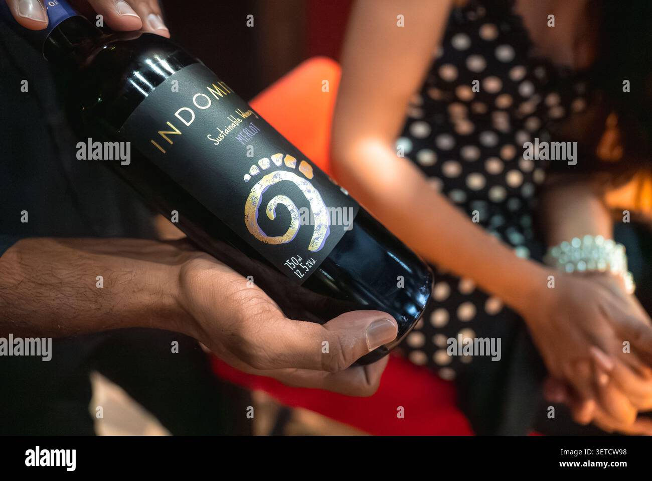 La persona presenta il flacone INDONI Zinfandel da 750 ML in una calda luce interna Foto Stock