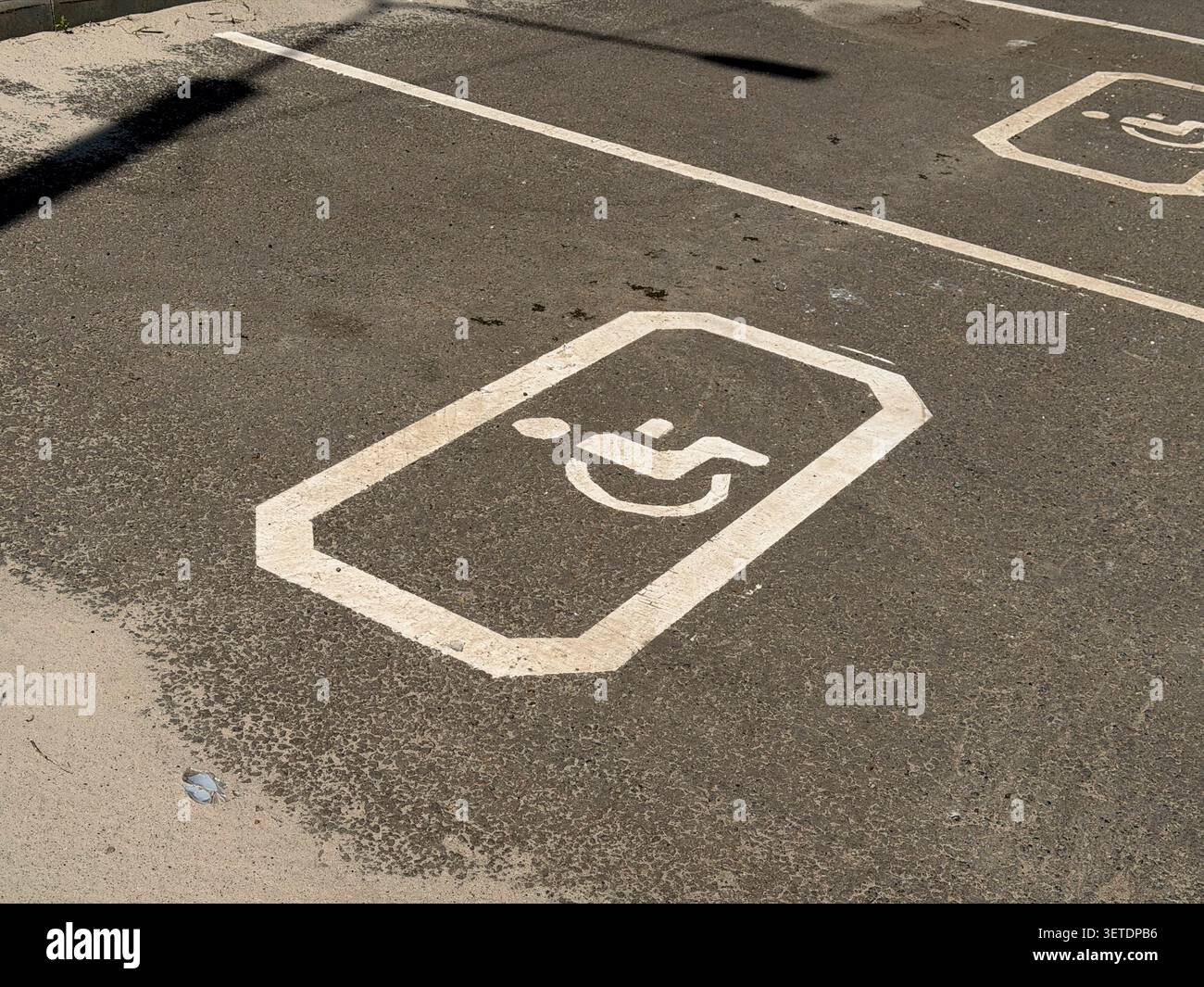 Simbolo di disabilità della sedia a rotelle verniciato di bianco su una superficie asfaltata che indica uno spazio di parcheggio designato. - Immagine stock catturata con smartphone
