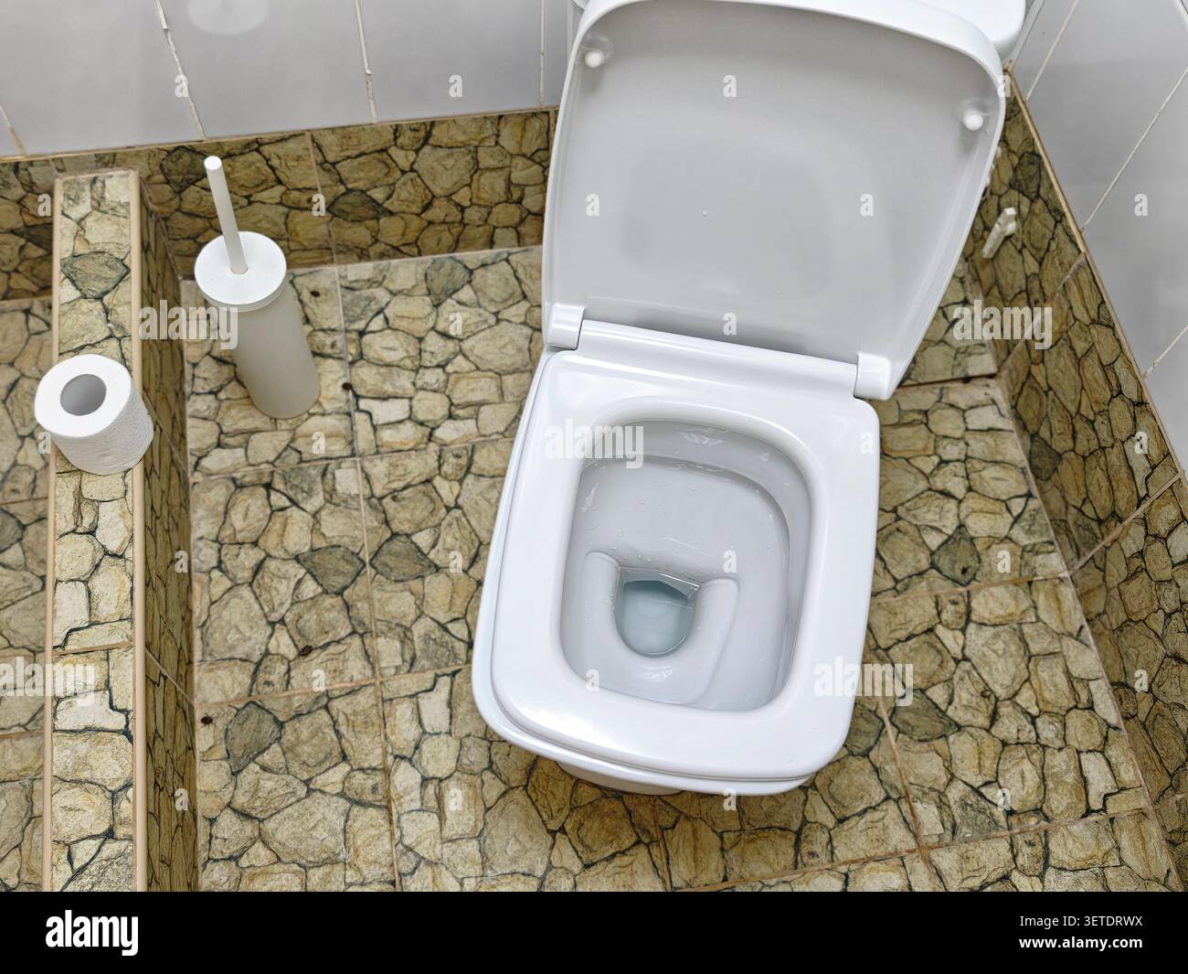 Una toilette pulita si trova su un pavimento in pietra in un bagno moderno. Lo spazio presenta un design semplice e funzioni pratiche per l'uso quotidiano. Foto Stock