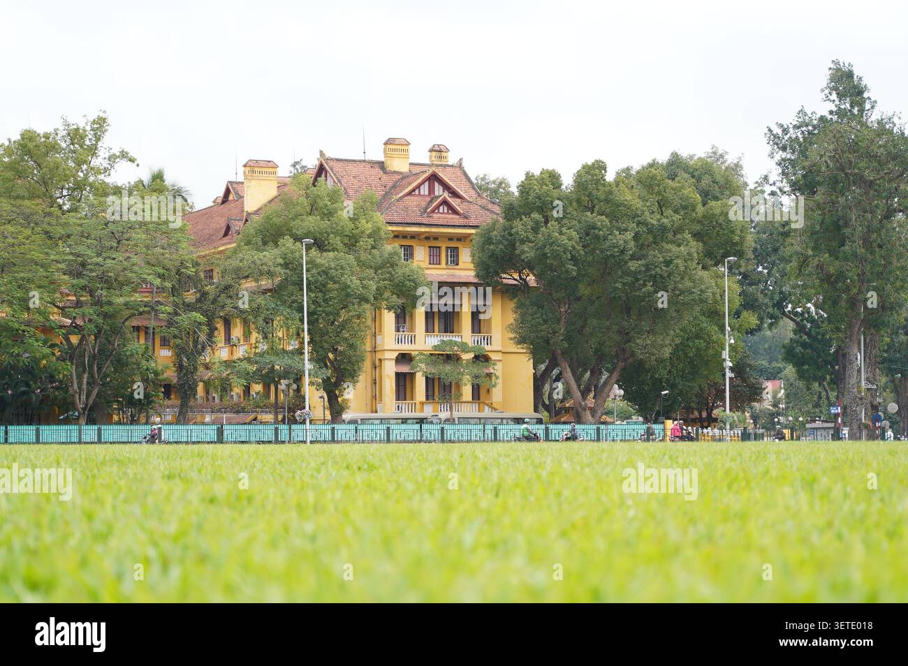 Storico palazzo presidenziale coloniale francese giallo ad Hanoi, Vietnam. Residenza d'epoca a due piani circondata da vasti prati verdi e alti alberi tropicali Foto Stock