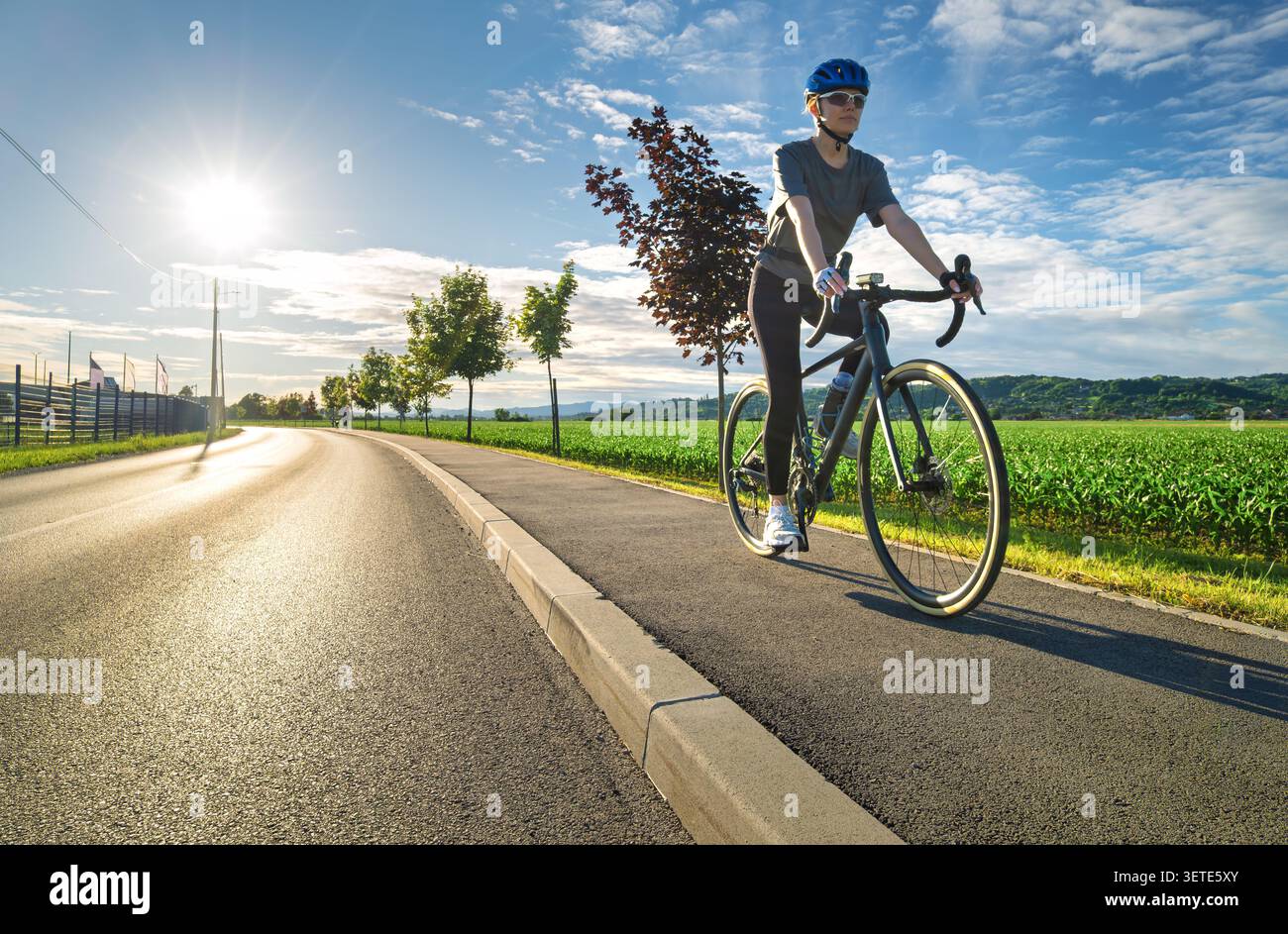 Ciclista donna con bici da strada in asfalto al tramonto Foto Stock