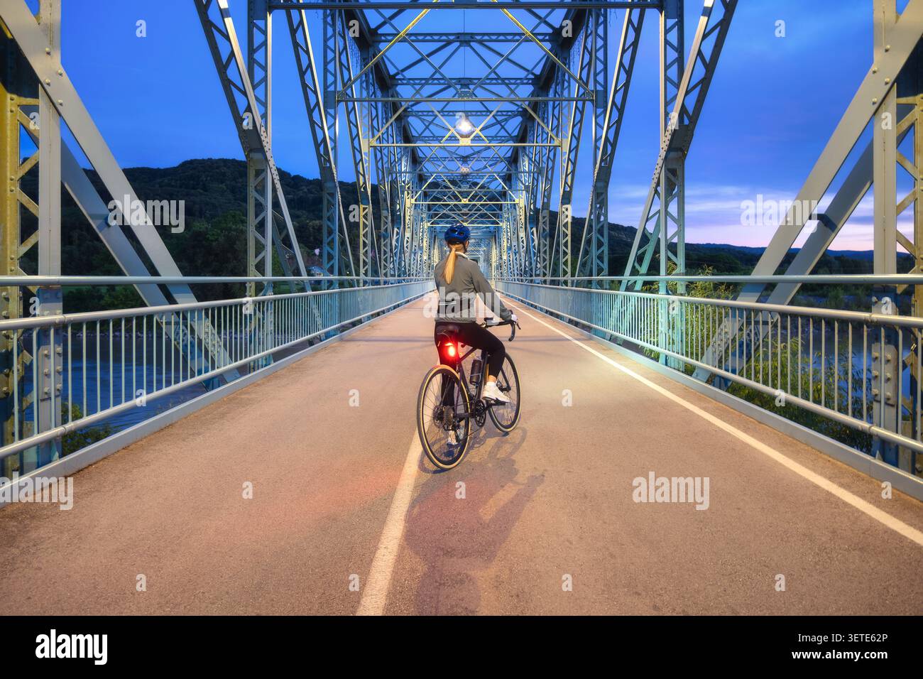 Ciclista donna con bici da strada su un ponte in metallo al crepuscolo Foto Stock