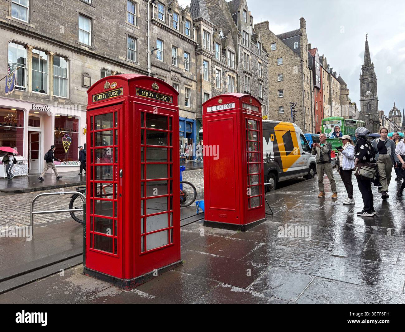 Due iconiche cabine telefoniche rosse sul Royal Mile, High Street, Edimburgo, Scozia. Edifici in pietra e pedoni fiancheggiano la strada bagnata. Foto Stock