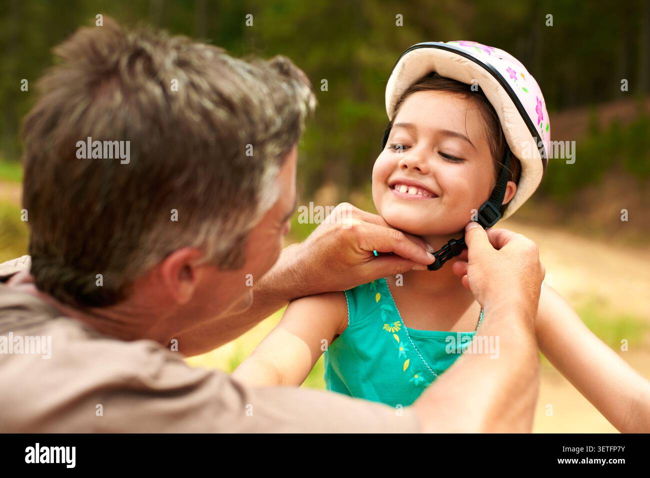 Sorridi, padre e aiuta il bambino con casco, sicurezza e guida per andare in bicicletta. Felice, uomo e figlia in natura con equipaggiamento protettivo, ciclismo Foto Stock