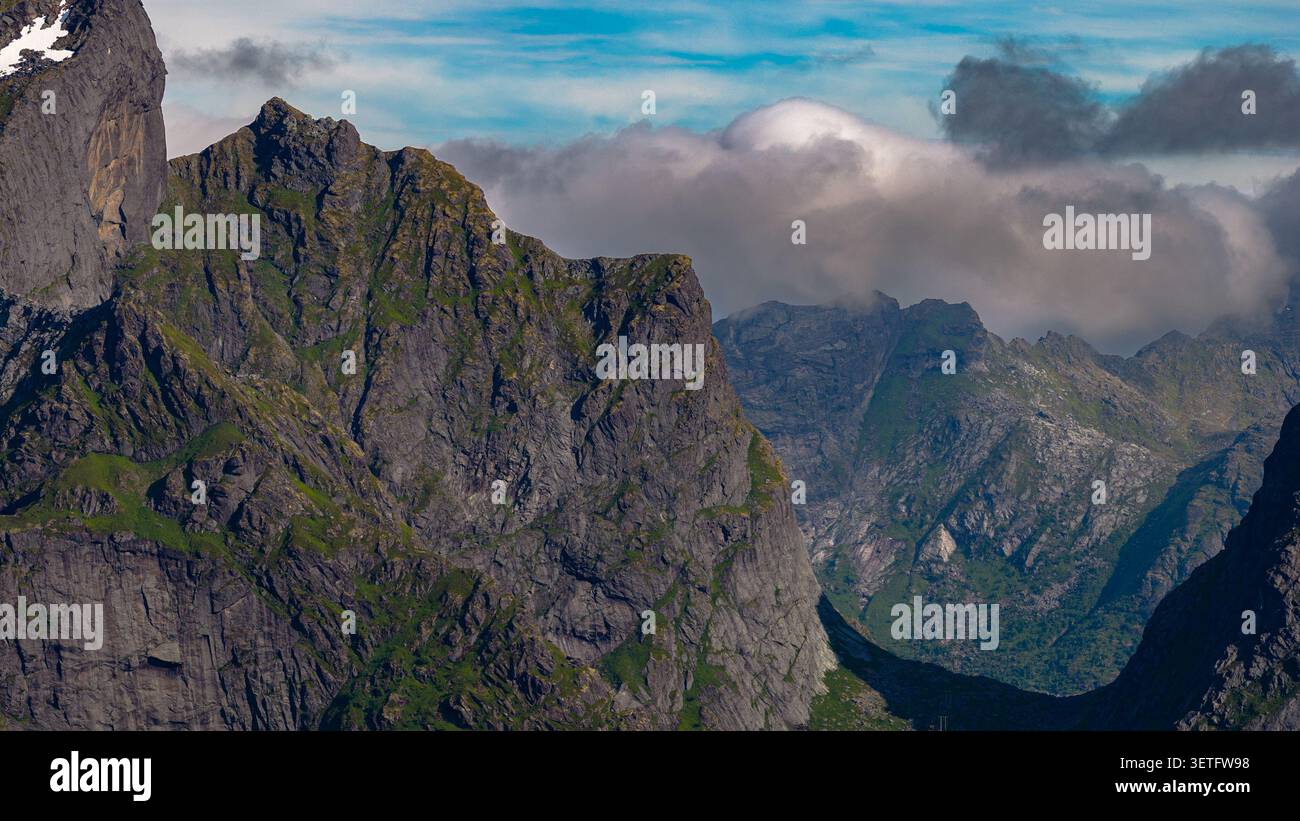 Maestosa valle alpina a Lofoten, Norvegia, con torreggianti scogliere di granito, lussureggianti pendii verdi e suggestive vette di montagna avvolte Foto Stock