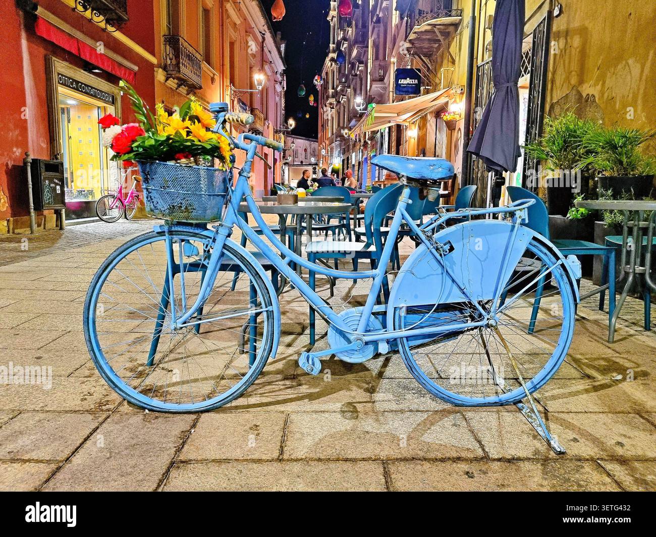 Scena notturna di una strada pittoresca con una bicicletta blu decorativa a Oristano, Sardegna, Italia Foto Stock