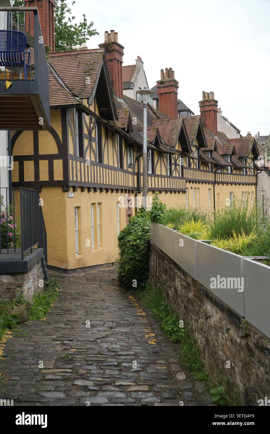 Storico edificio in legno incorniciato nel Dean Village, Edimburgo. Sentiero acciottolato e pareti gialle rese sotto un cielo coperto. Foto Stock