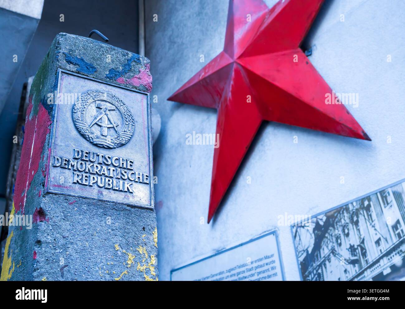 Storico marcatore di confine con l'emblema di stato dell'ex Repubblica Democratica tedesca (DDR) esposto accanto a una stella socialista rossa a Berlino. Foto Stock