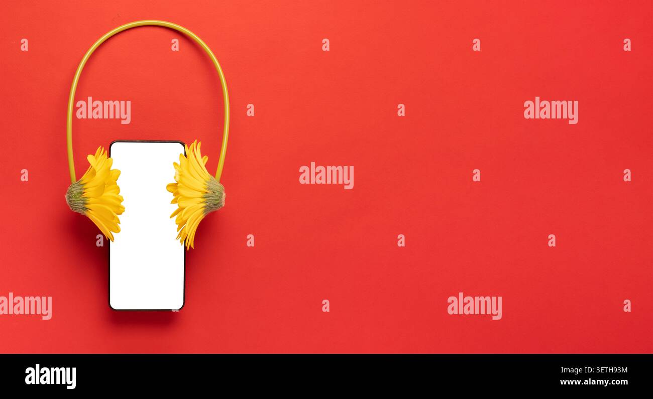 Composizione creativa di un mockup per smartphone con cuffie gialle a fiori su sfondo rosso brillante con spazio di copia. Concetto di app musicale, podcast e au Foto Stock