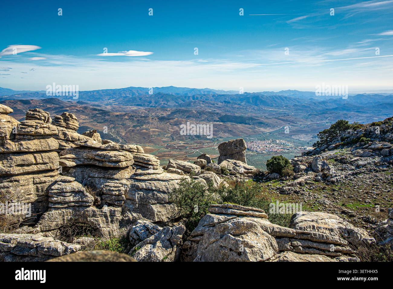 Formazioni rocciose calcaree e paesaggio carsico a El Torcal vicino ad Antequera in Andalusia, Spagna, con un'ampia vista su una valle asciutta, un villaggio lontano e. Foto Stock